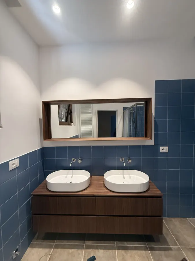 Mobile sospeso color legno con due lavabi bianchi e specchio su rivestimento blu
