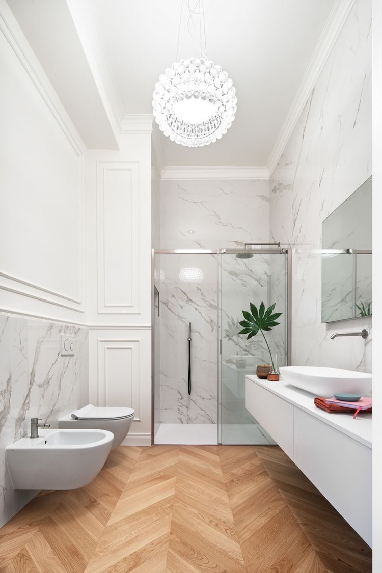 Bagno con rivestimento chiaro effetto marmo e pavimento color legno a spina di pesce